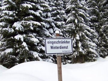Schild "eingeschränkter Winterdienst" vor Winterlandschaft